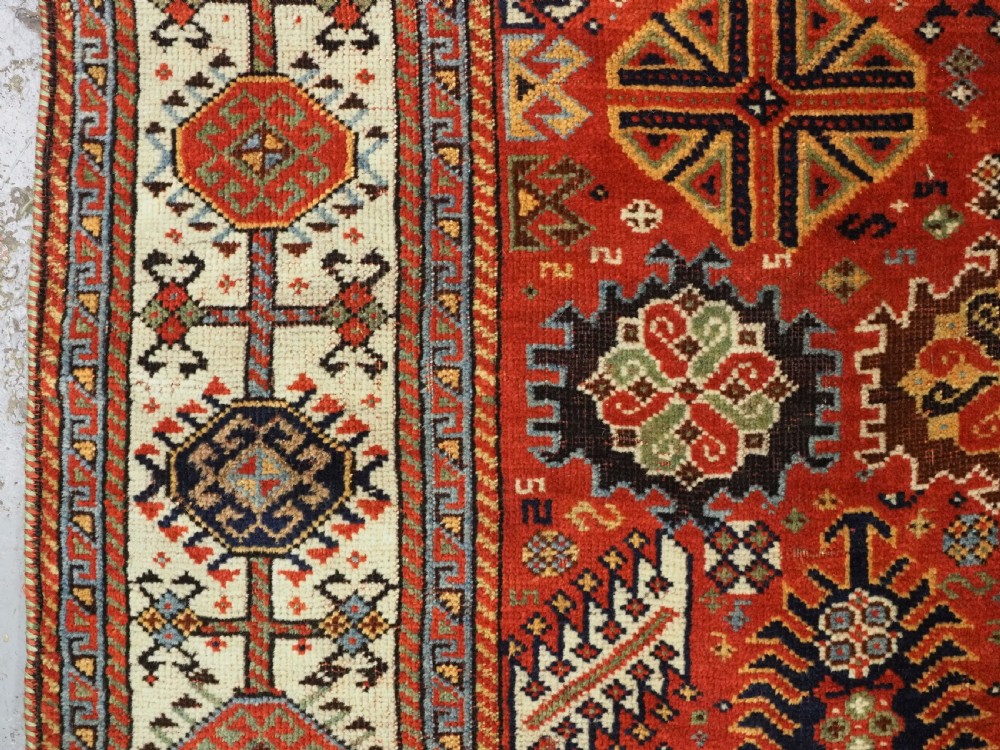 An antique South Persian Shekarlu Qashqai wool rug featuring a red field with dense geometric tribal motifs surrounded by an ivory patterned border. View V