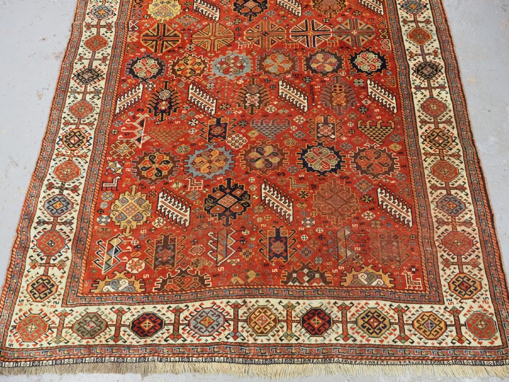 An antique South Persian Shekarlu Qashqai wool rug featuring a red field with dense geometric tribal motifs surrounded by an ivory patterned border. View VI