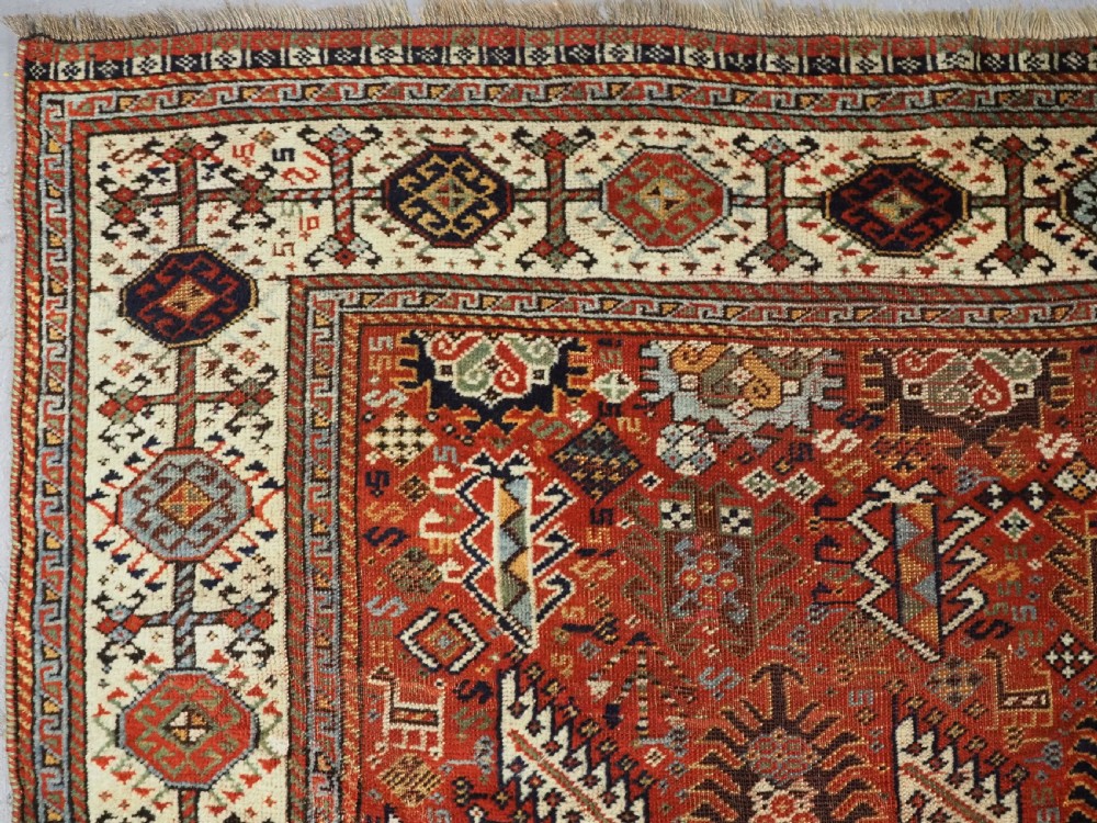 An antique South Persian Shekarlu Qashqai wool rug featuring a red field with dense geometric tribal motifs surrounded by an ivory patterned border. View VII