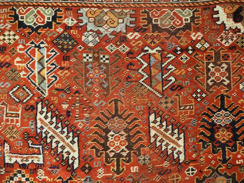 An antique South Persian Shekarlu Qashqai wool rug featuring a red field with dense geometric tribal motifs surrounded by an ivory patterned border. View VIII