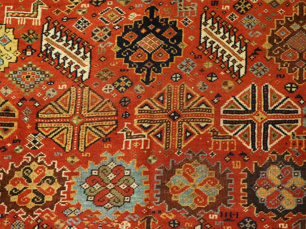 An antique South Persian Shekarlu Qashqai wool rug featuring a red field with dense geometric tribal motifs surrounded by an ivory patterned border. View X