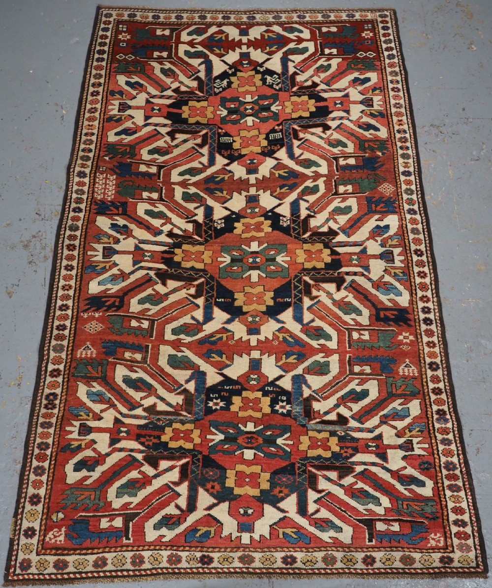 An antique Caucasian Chelaberd Kazak wool rug featuring three prominent sunburst medallions in cream, navy, and green set against a bold red ground with geometric borders.