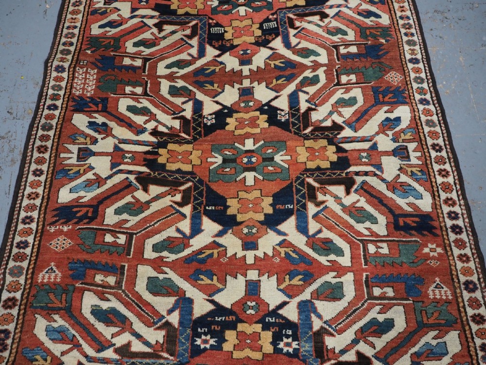 An antique Caucasian Chelaberd Kazak wool rug featuring three prominent sunburst medallions in cream, navy, and green set against a bold red ground with geometric borders. View III