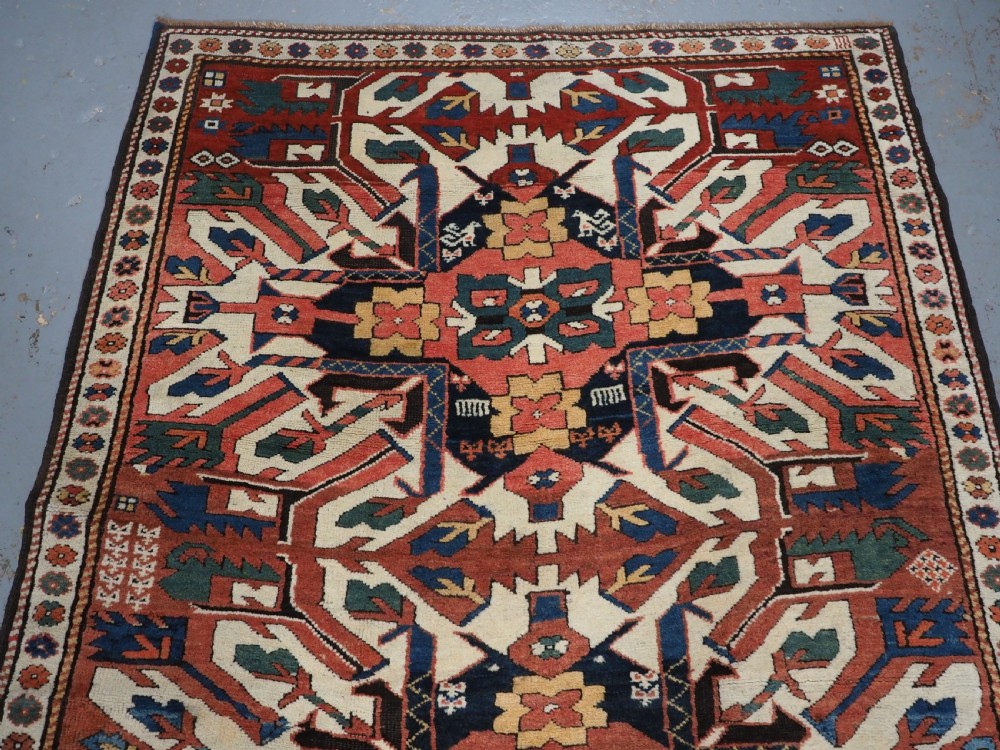 An antique Caucasian Chelaberd Kazak wool rug featuring three prominent sunburst medallions in cream, navy, and green set against a bold red ground with geometric borders. View IV