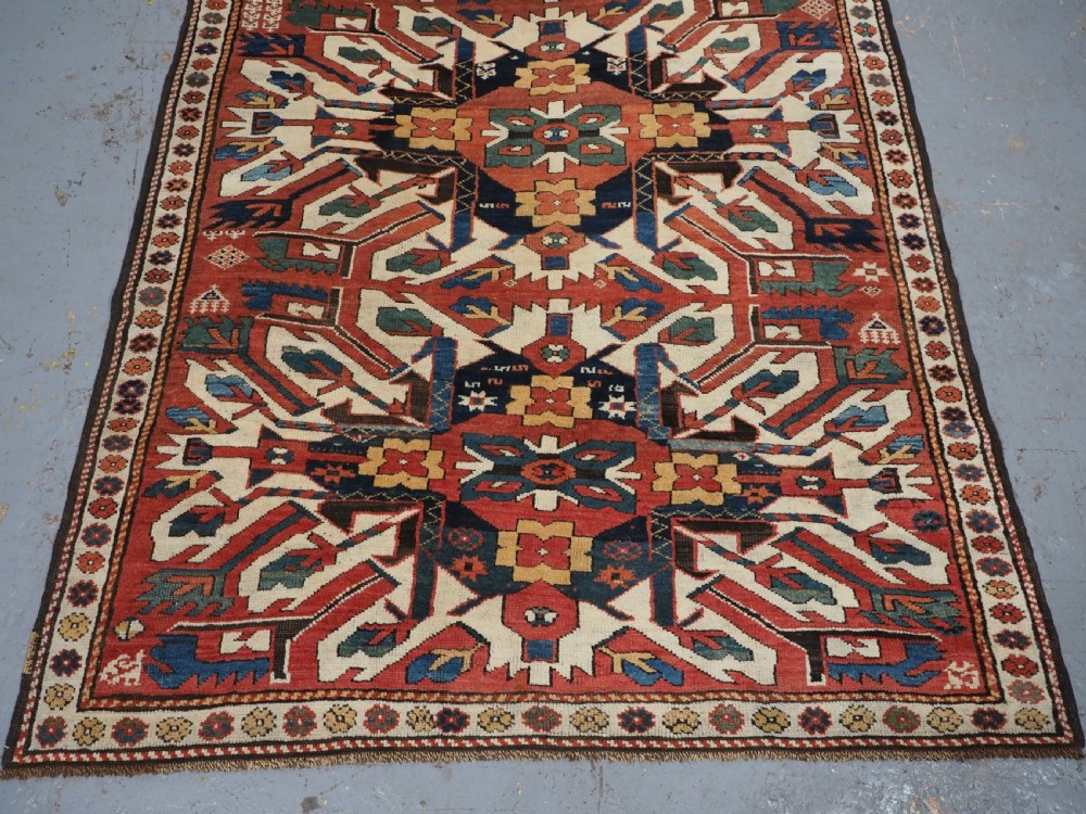 An antique Caucasian Chelaberd Kazak wool rug featuring three prominent sunburst medallions in cream, navy, and green set against a bold red ground with geometric borders. View V