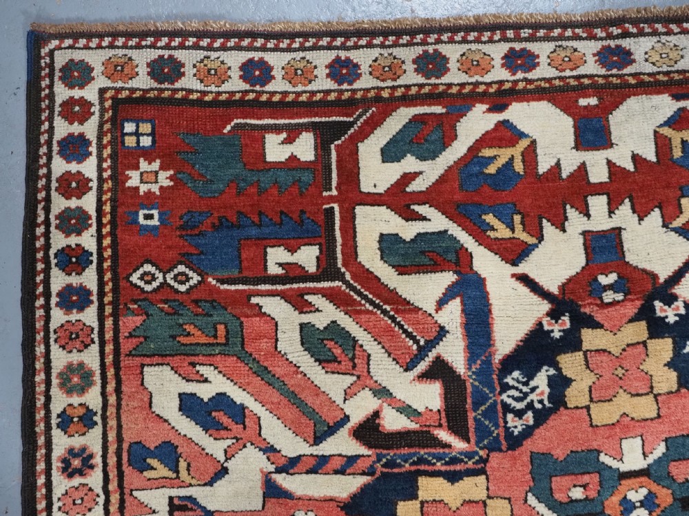 An antique Caucasian Chelaberd Kazak wool rug featuring three prominent sunburst medallions in cream, navy, and green set against a bold red ground with geometric borders. View VI