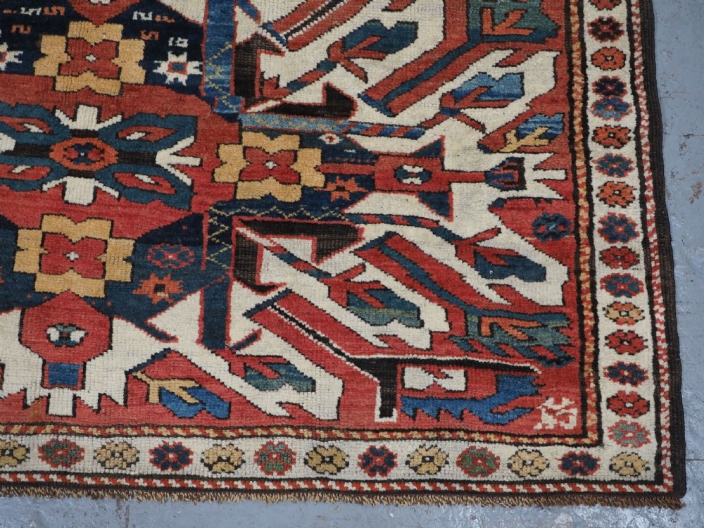 An antique Caucasian Chelaberd Kazak wool rug featuring three prominent sunburst medallions in cream, navy, and green set against a bold red ground with geometric borders. View IX