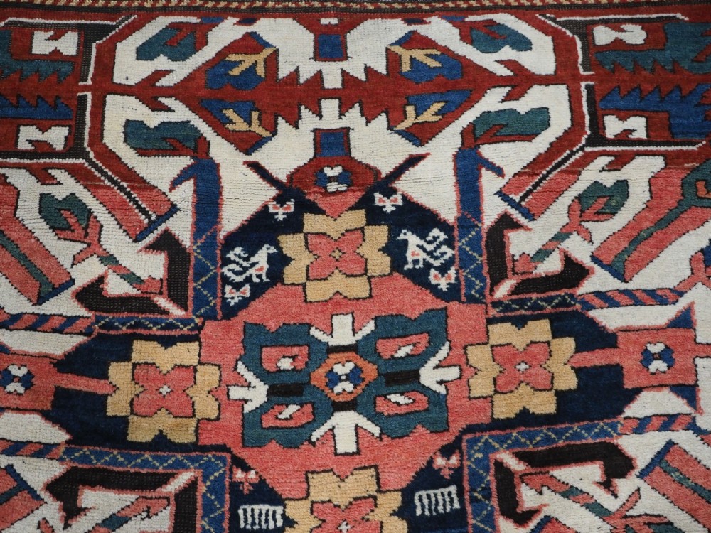 An antique Caucasian Chelaberd Kazak wool rug featuring three prominent sunburst medallions in cream, navy, and green set against a bold red ground with geometric borders. View XI