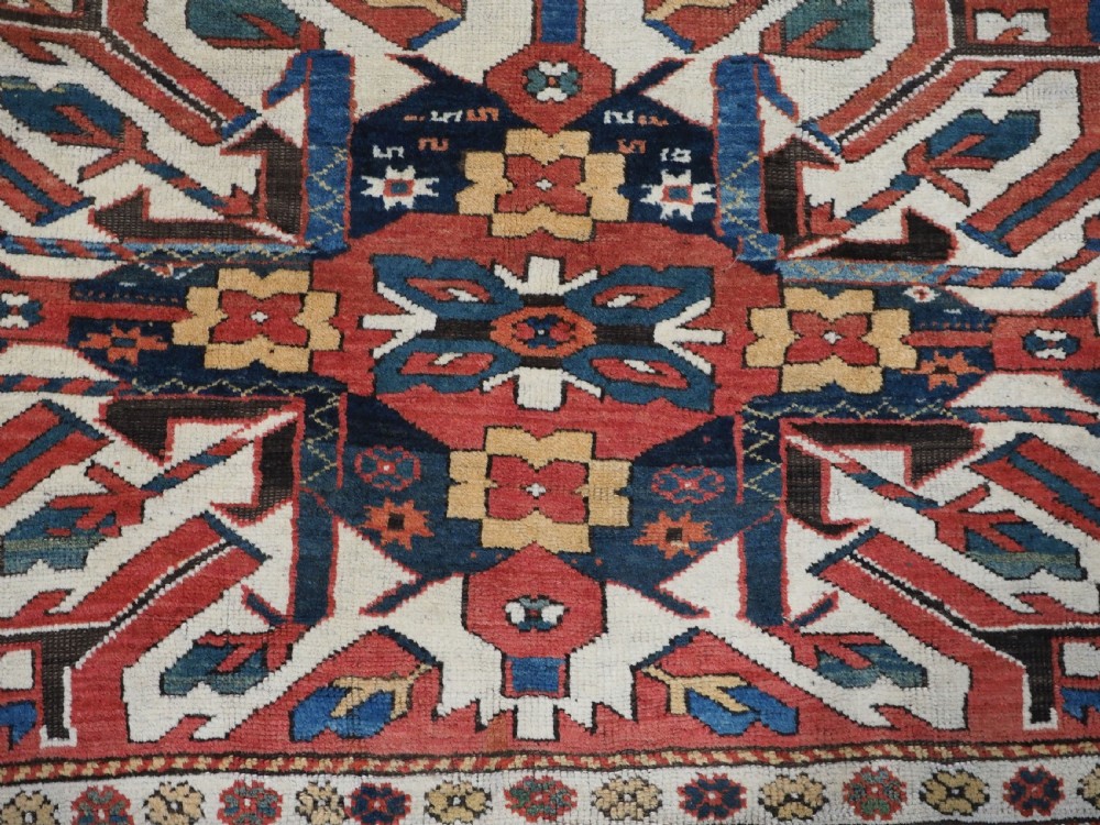 An antique Caucasian Chelaberd Kazak wool rug featuring three prominent sunburst medallions in cream, navy, and green set against a bold red ground with geometric borders. View XV
