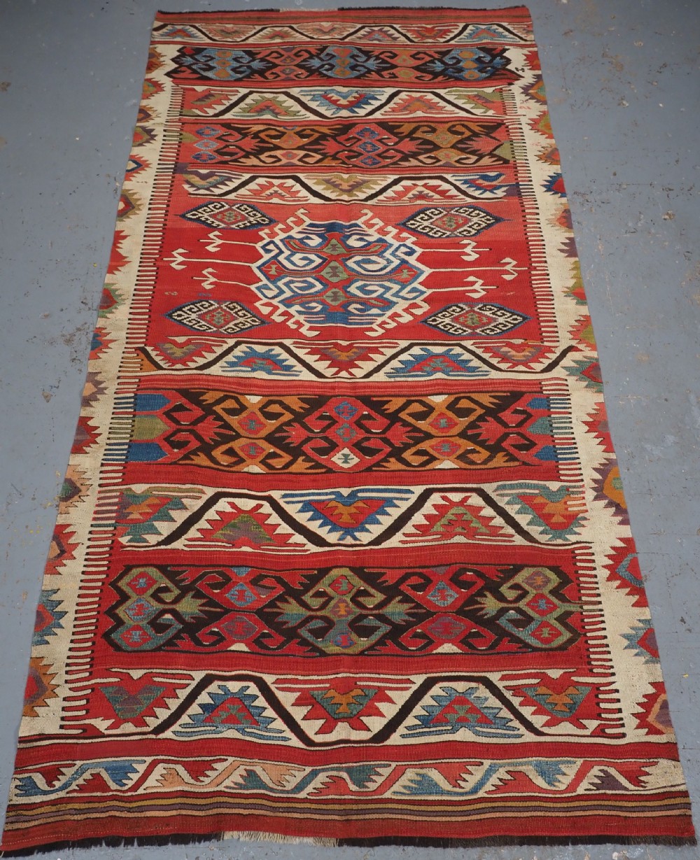 A long hand-woven Turkish Mut kilim rug featuring bold red, navy, brown, and cream geometric motifs arranged in horizontal bands.