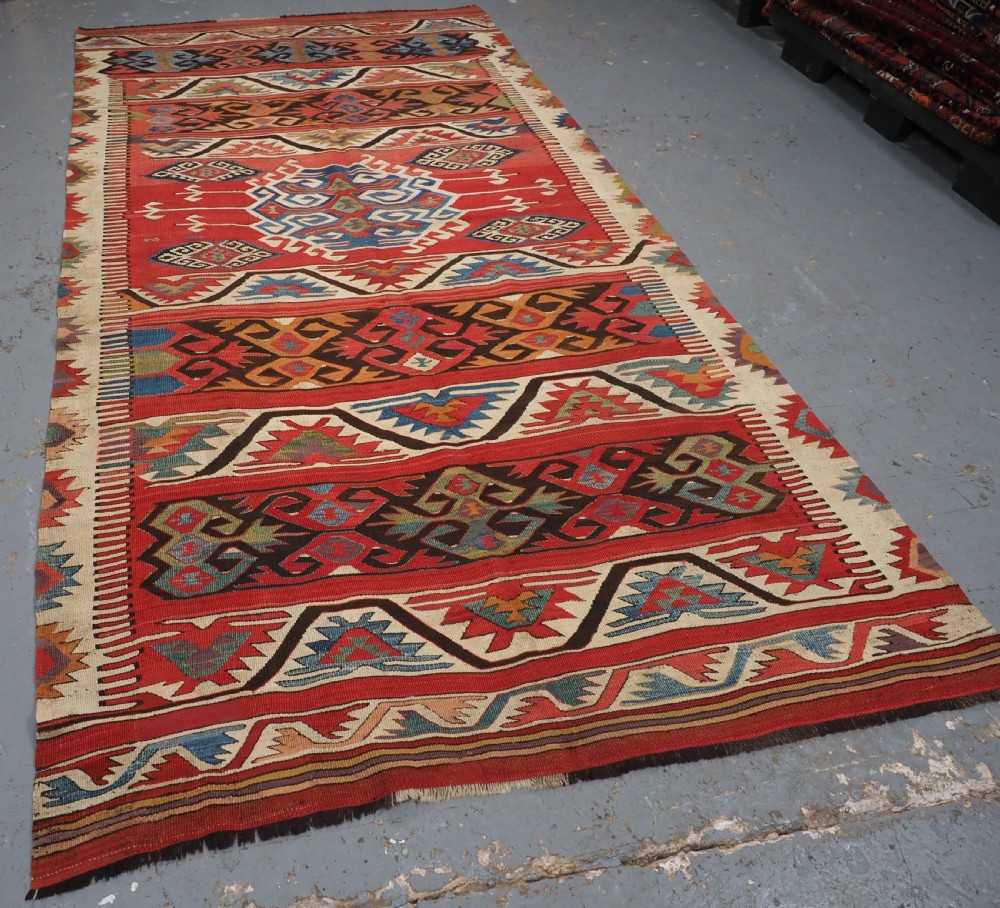A long hand-woven Turkish Mut kilim rug featuring bold red, navy, brown, and cream geometric motifs arranged in horizontal bands. View II
