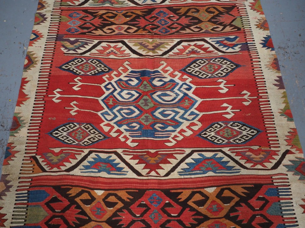 A long hand-woven Turkish Mut kilim rug featuring bold red, navy, brown, and cream geometric motifs arranged in horizontal bands. View IV