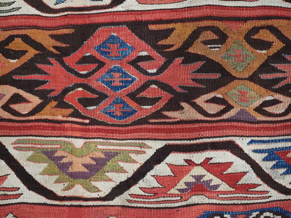 A long hand-woven Turkish Mut kilim rug featuring bold red, navy, brown, and cream geometric motifs arranged in horizontal bands. View VII