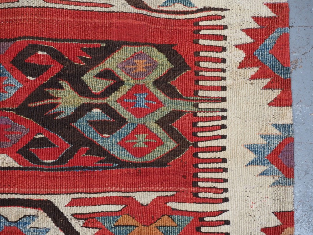 A long hand-woven Turkish Mut kilim rug featuring bold red, navy, brown, and cream geometric motifs arranged in horizontal bands. View X