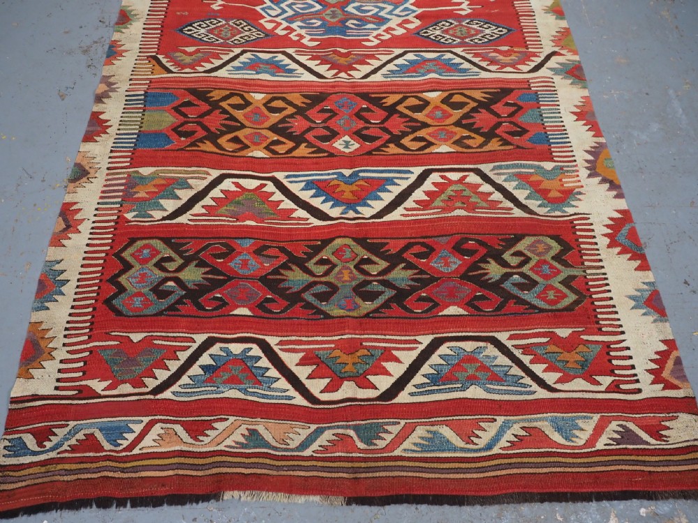 A long hand-woven Turkish Mut kilim rug featuring bold red, navy, brown, and cream geometric motifs arranged in horizontal bands. View XI