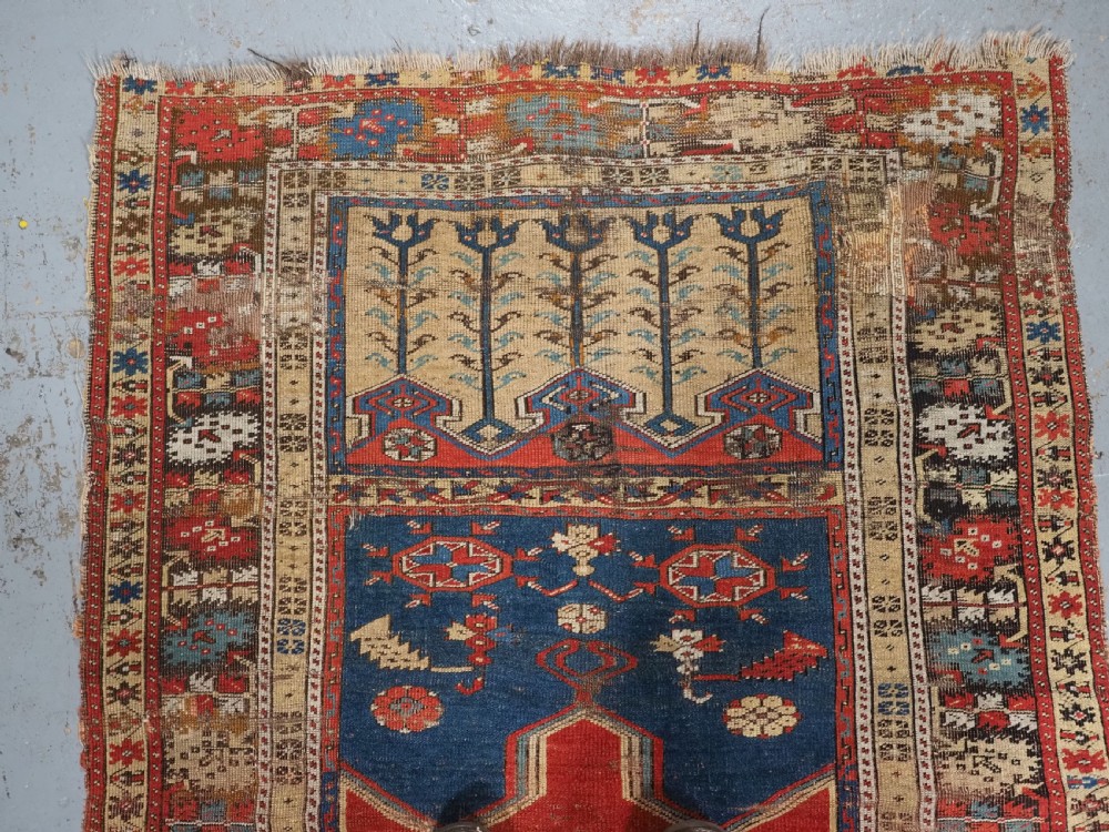 An antique hand-knotted Turkish Ladik prayer rug featuring a central red arched mihrab niche, blue spandrels, stylized floral panels, and a patterned multi-tiered border. View III