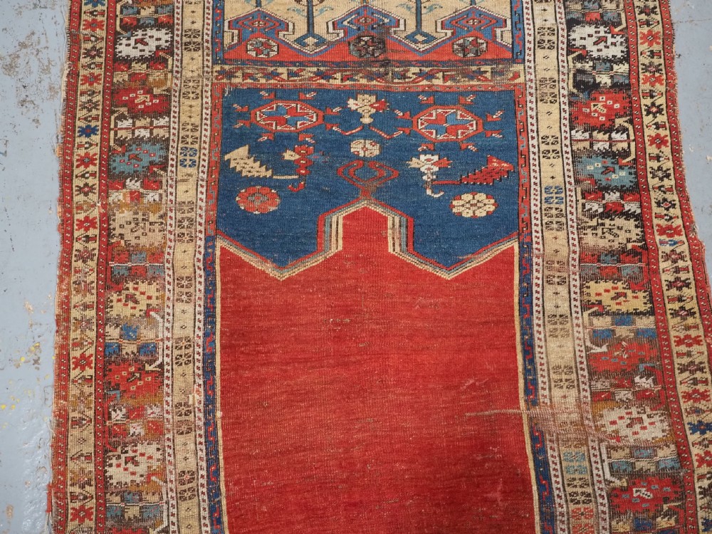 An antique hand-knotted Turkish Ladik prayer rug featuring a central red arched mihrab niche, blue spandrels, stylized floral panels, and a patterned multi-tiered border. View IV