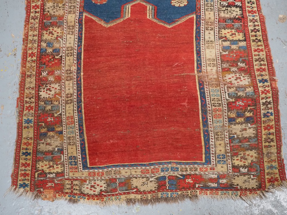 An antique hand-knotted Turkish Ladik prayer rug featuring a central red arched mihrab niche, blue spandrels, stylized floral panels, and a patterned multi-tiered border. View V