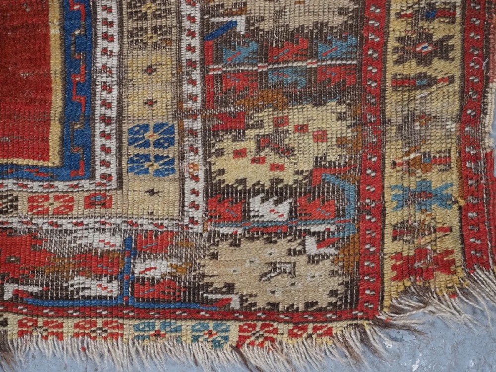An antique hand-knotted Turkish Ladik prayer rug featuring a central red arched mihrab niche, blue spandrels, stylized floral panels, and a patterned multi-tiered border. View VII