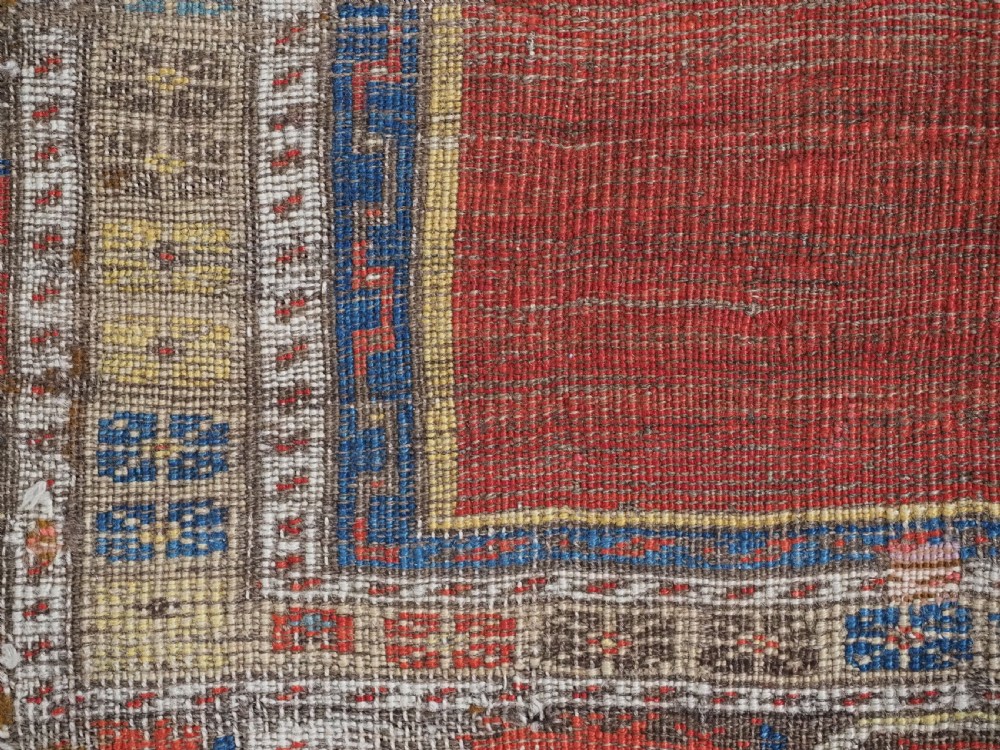 An antique hand-knotted Turkish Ladik prayer rug featuring a central red arched mihrab niche, blue spandrels, stylized floral panels, and a patterned multi-tiered border. View VIII