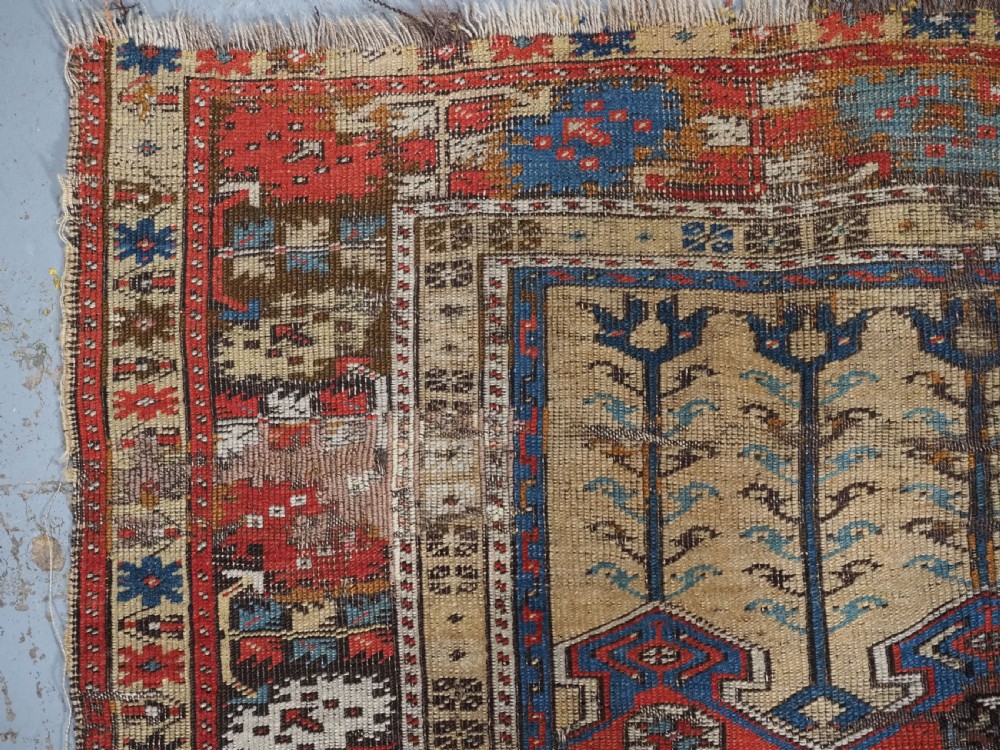 An antique hand-knotted Turkish Ladik prayer rug featuring a central red arched mihrab niche, blue spandrels, stylized floral panels, and a patterned multi-tiered border. View IX