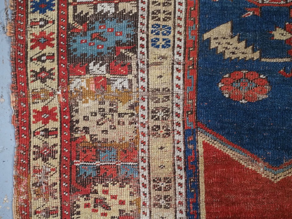 An antique hand-knotted Turkish Ladik prayer rug featuring a central red arched mihrab niche, blue spandrels, stylized floral panels, and a patterned multi-tiered border. View X