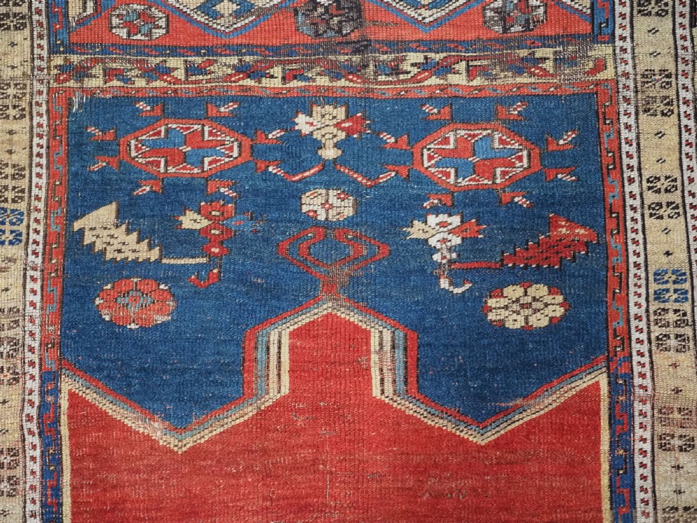 An antique hand-knotted Turkish Ladik prayer rug featuring a central red arched mihrab niche, blue spandrels, stylized floral panels, and a patterned multi-tiered border. View XII