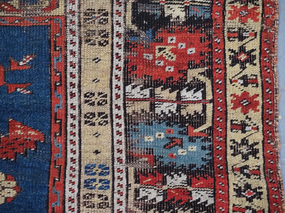 An antique hand-knotted Turkish Ladik prayer rug featuring a central red arched mihrab niche, blue spandrels, stylized floral panels, and a patterned multi-tiered border. View XV