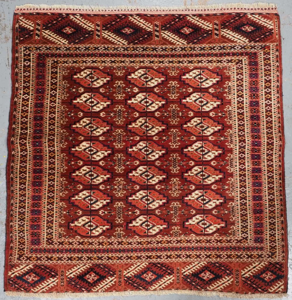 A rectangular handwoven Tekke Turkmen wool rug featuring repeating primary gul motifs in deep red, navy, terracotta, and ivory tones surrounded by geometric borders.