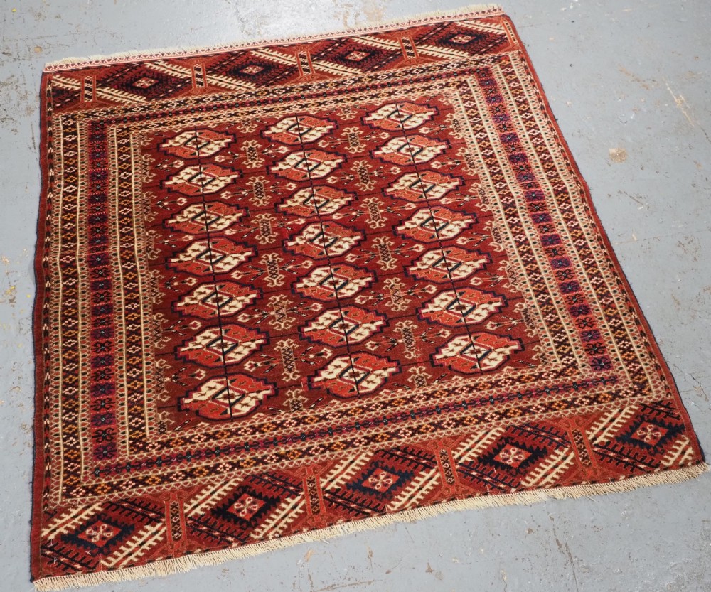 A rectangular handwoven Tekke Turkmen wool rug featuring repeating primary gul motifs in deep red, navy, terracotta, and ivory tones surrounded by geometric borders. View II