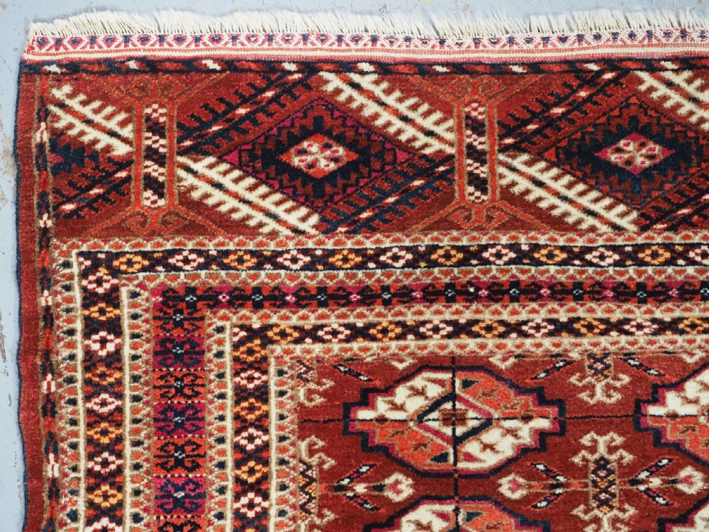 A rectangular handwoven Tekke Turkmen wool rug featuring repeating primary gul motifs in deep red, navy, terracotta, and ivory tones surrounded by geometric borders. View V