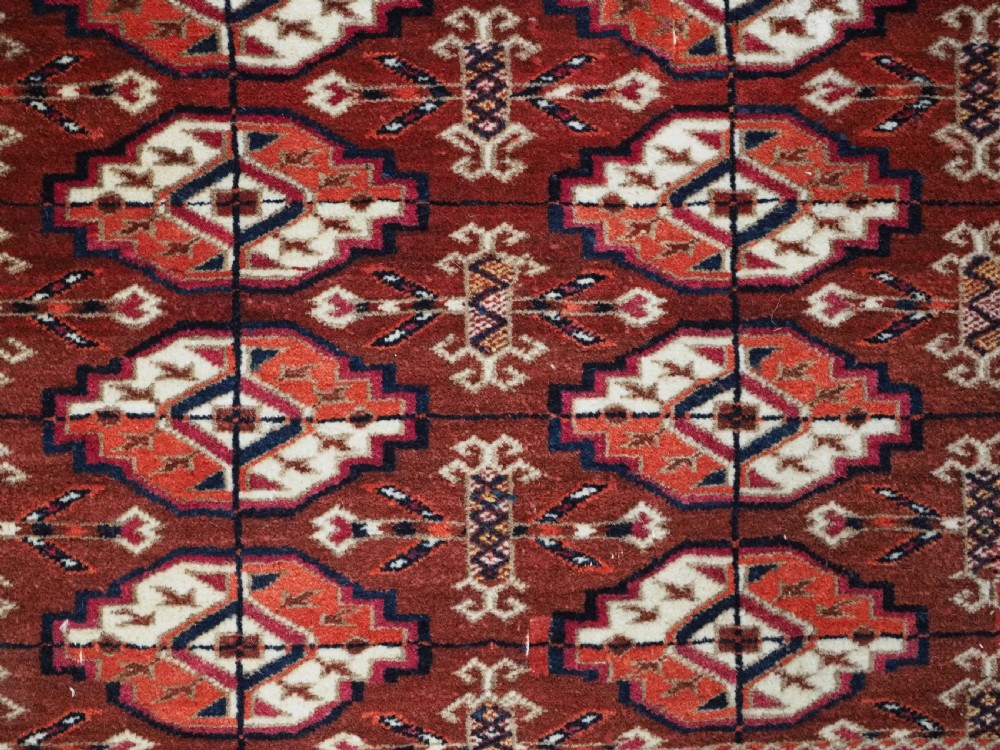 A rectangular handwoven Tekke Turkmen wool rug featuring repeating primary gul motifs in deep red, navy, terracotta, and ivory tones surrounded by geometric borders. View VIII