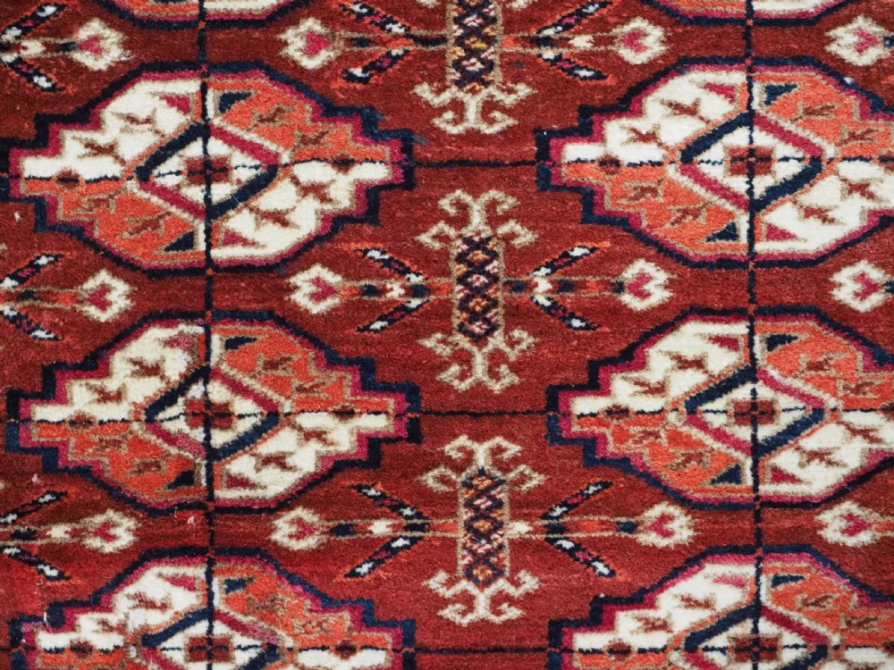 A rectangular handwoven Tekke Turkmen wool rug featuring repeating primary gul motifs in deep red, navy, terracotta, and ivory tones surrounded by geometric borders. View IX