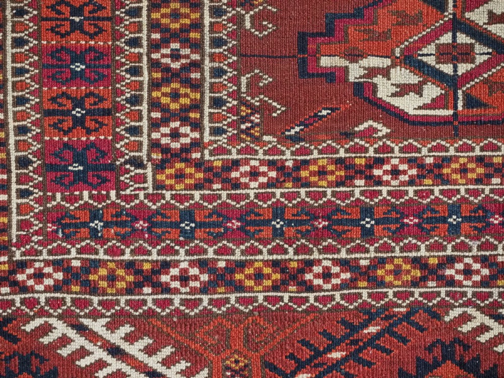 A rectangular handwoven Tekke Turkmen wool rug featuring repeating primary gul motifs in deep red, navy, terracotta, and ivory tones surrounded by geometric borders. View XI