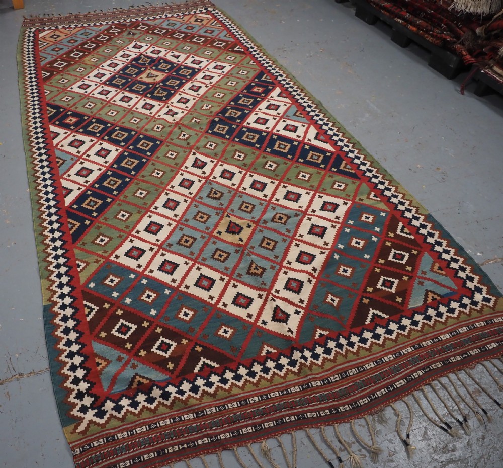 An antique Persian Qashqai tribal kilim rug featuring a dense geometric diamond lattice pattern in terracotta, navy blue, sage green, and cream wool with fringed ends. View II
