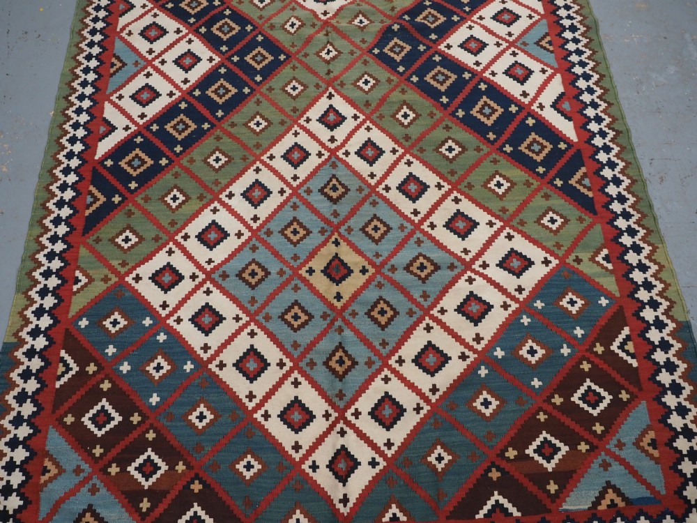 An antique Persian Qashqai tribal kilim rug featuring a dense geometric diamond lattice pattern in terracotta, navy blue, sage green, and cream wool with fringed ends. View V