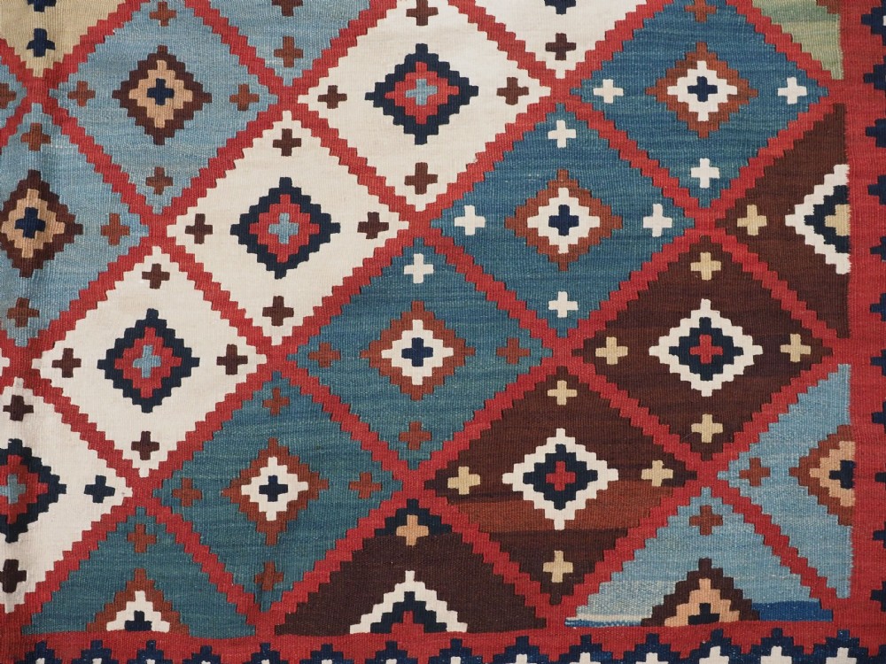 An antique Persian Qashqai tribal kilim rug featuring a dense geometric diamond lattice pattern in terracotta, navy blue, sage green, and cream wool with fringed ends. View VI