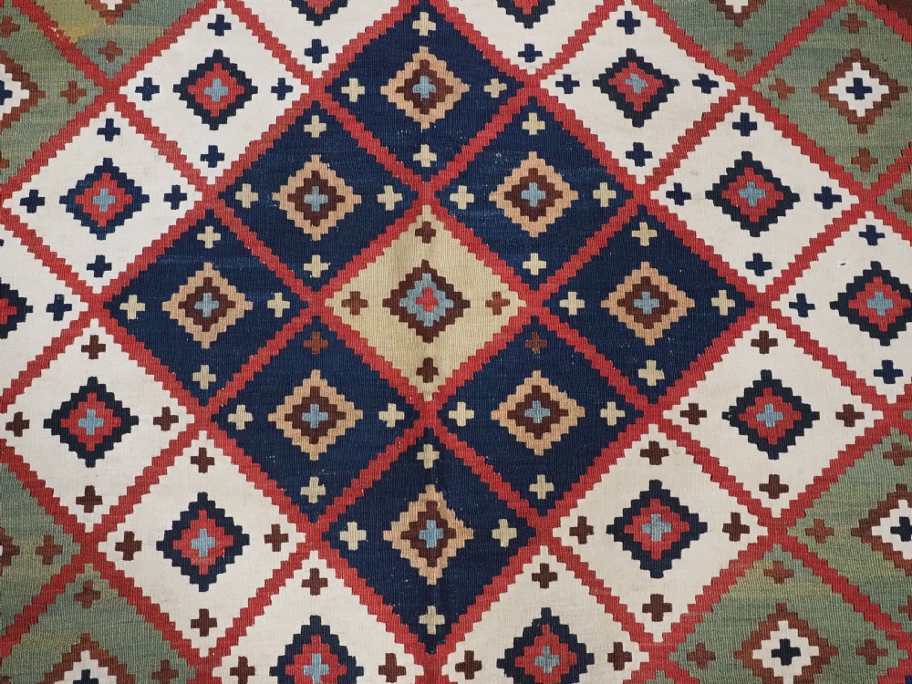 An antique Persian Qashqai tribal kilim rug featuring a dense geometric diamond lattice pattern in terracotta, navy blue, sage green, and cream wool with fringed ends. View VII