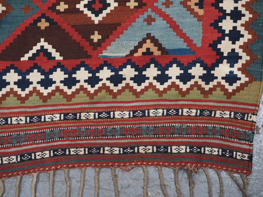An antique Persian Qashqai tribal kilim rug featuring a dense geometric diamond lattice pattern in terracotta, navy blue, sage green, and cream wool with fringed ends. View VIII