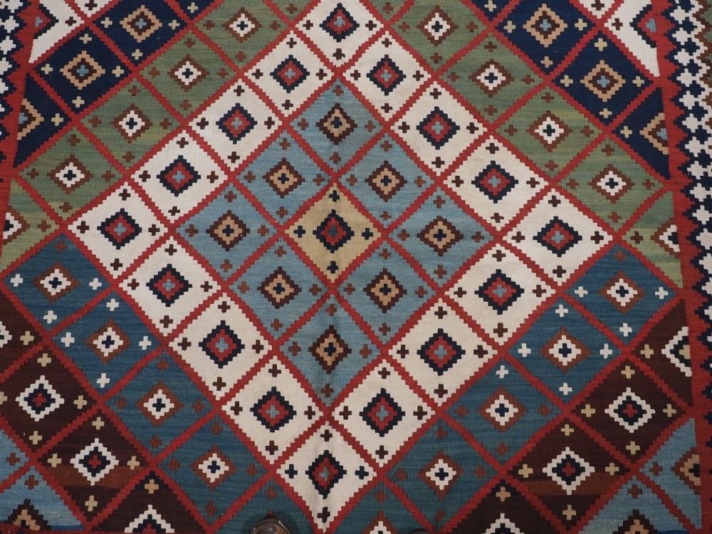 An antique Persian Qashqai tribal kilim rug featuring a dense geometric diamond lattice pattern in terracotta, navy blue, sage green, and cream wool with fringed ends. View IX
