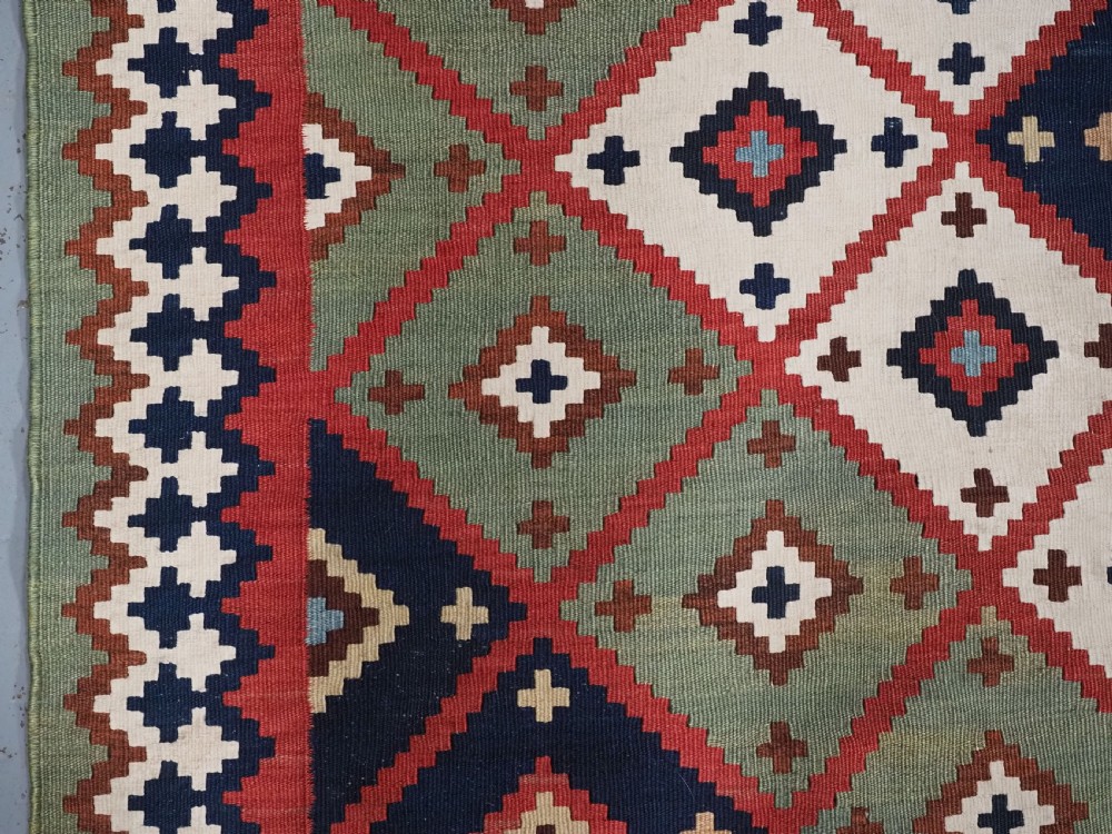 An antique Persian Qashqai tribal kilim rug featuring a dense geometric diamond lattice pattern in terracotta, navy blue, sage green, and cream wool with fringed ends. View XII