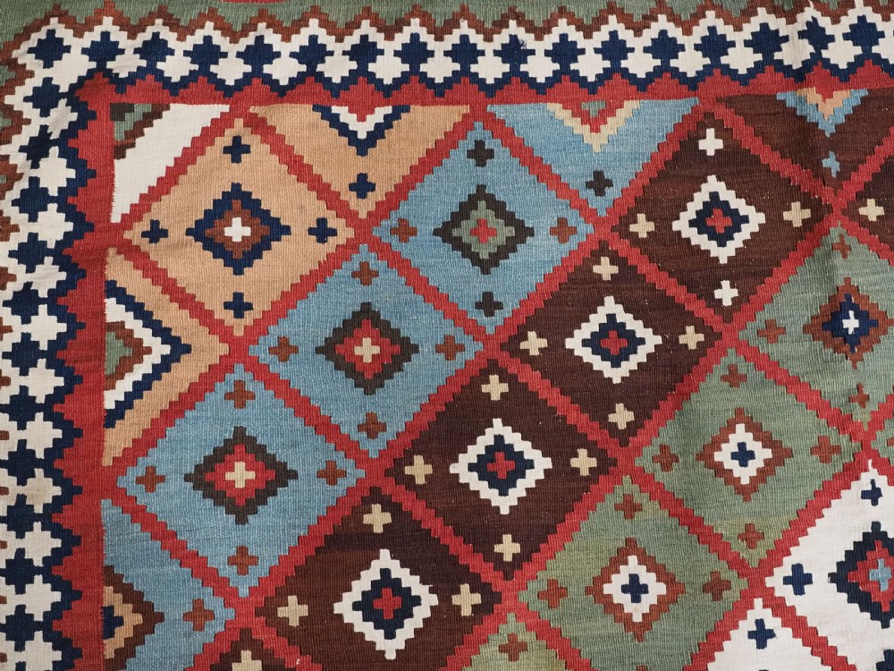 An antique Persian Qashqai tribal kilim rug featuring a dense geometric diamond lattice pattern in terracotta, navy blue, sage green, and cream wool with fringed ends. View XIV