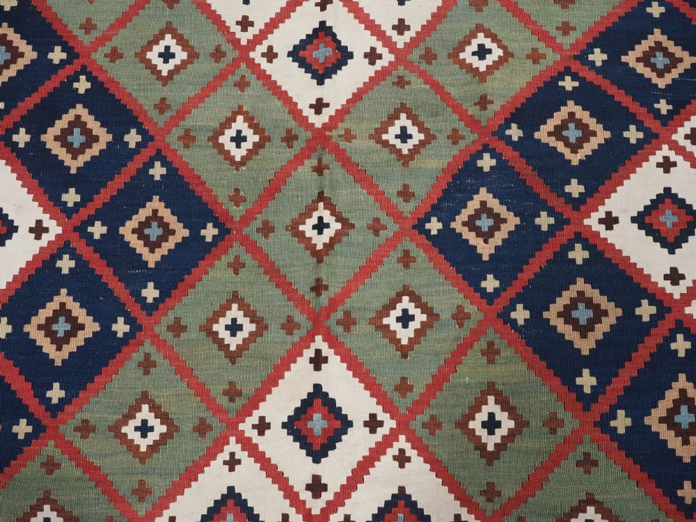 An antique Persian Qashqai tribal kilim rug featuring a dense geometric diamond lattice pattern in terracotta, navy blue, sage green, and cream wool with fringed ends. View XV
