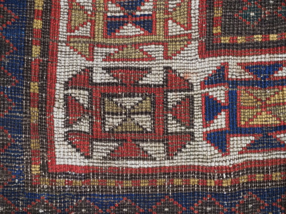 An antique hand-knotted Caucasian rug featuring geometric diamond medallions and folk art figures on a deep red wool field. View XIX