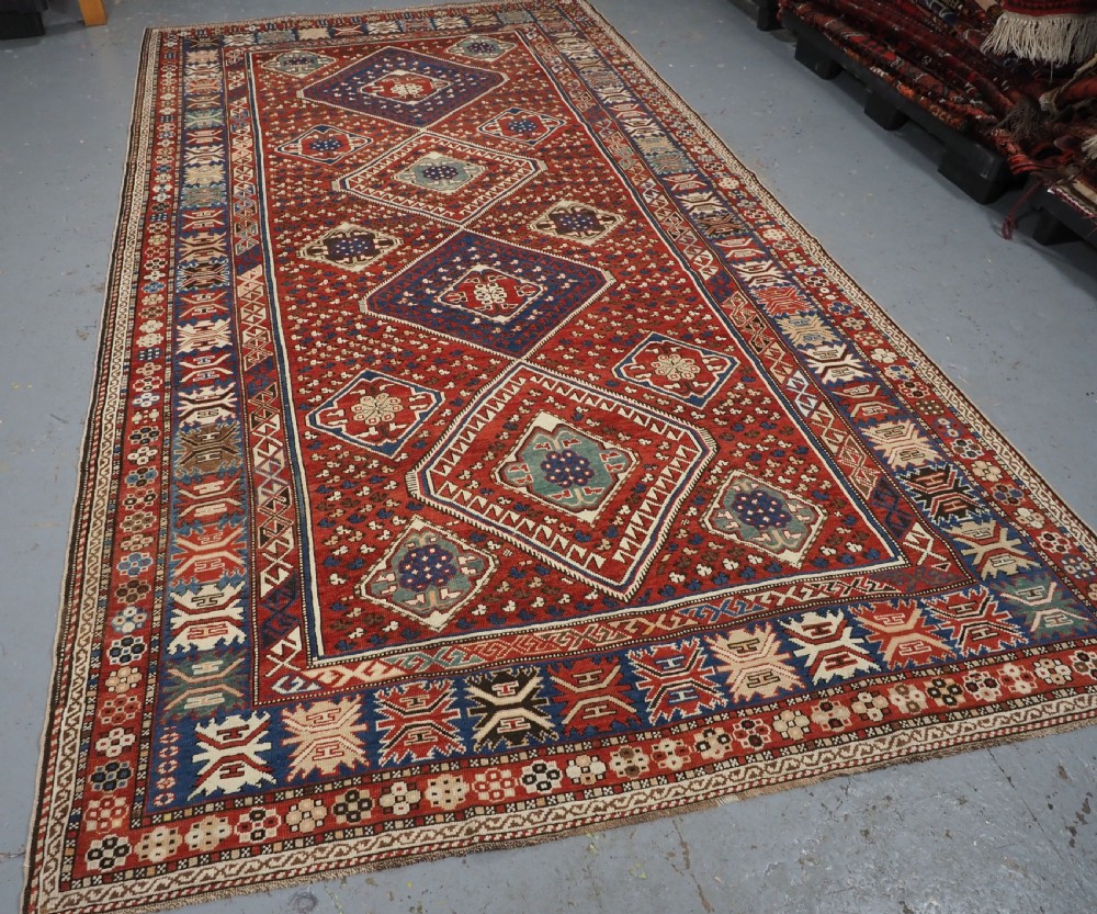 An antique hand-knotted Caucasian Shirvan Baku Khila wool rug featuring geometric diamond medallions on a red ground with navy blue and ivory borders. View II