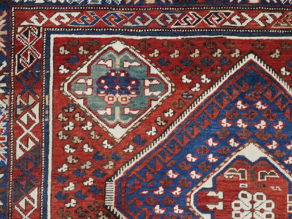 An antique hand-knotted Caucasian Shirvan Baku Khila wool rug featuring geometric diamond medallions on a red ground with navy blue and ivory borders. View VII