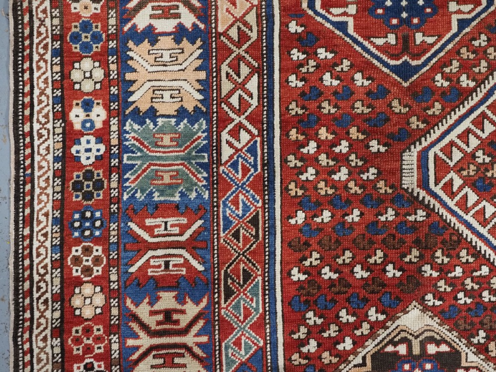 An antique hand-knotted Caucasian Shirvan Baku Khila wool rug featuring geometric diamond medallions on a red ground with navy blue and ivory borders. View VIII