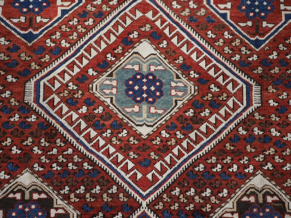 An antique hand-knotted Caucasian Shirvan Baku Khila wool rug featuring geometric diamond medallions on a red ground with navy blue and ivory borders. View IX