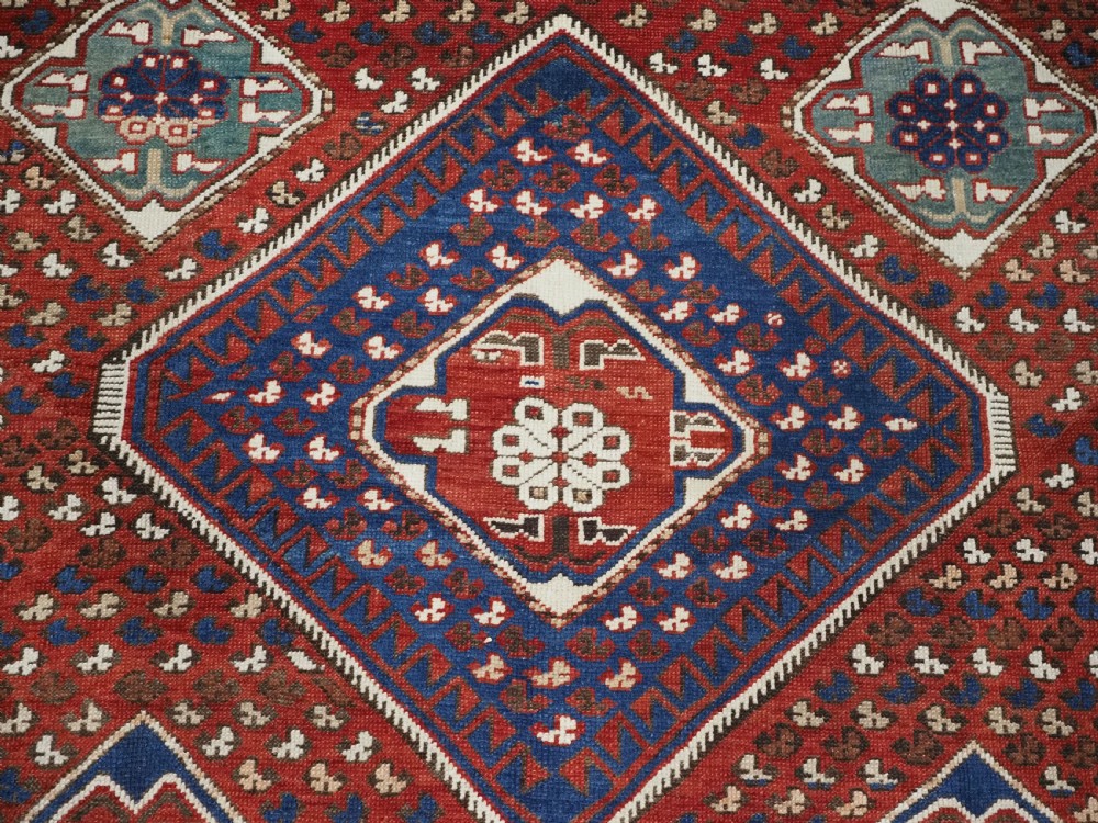 An antique hand-knotted Caucasian Shirvan Baku Khila wool rug featuring geometric diamond medallions on a red ground with navy blue and ivory borders. View X