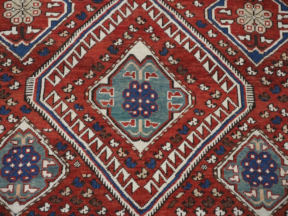 An antique hand-knotted Caucasian Shirvan Baku Khila wool rug featuring geometric diamond medallions on a red ground with navy blue and ivory borders. View XII